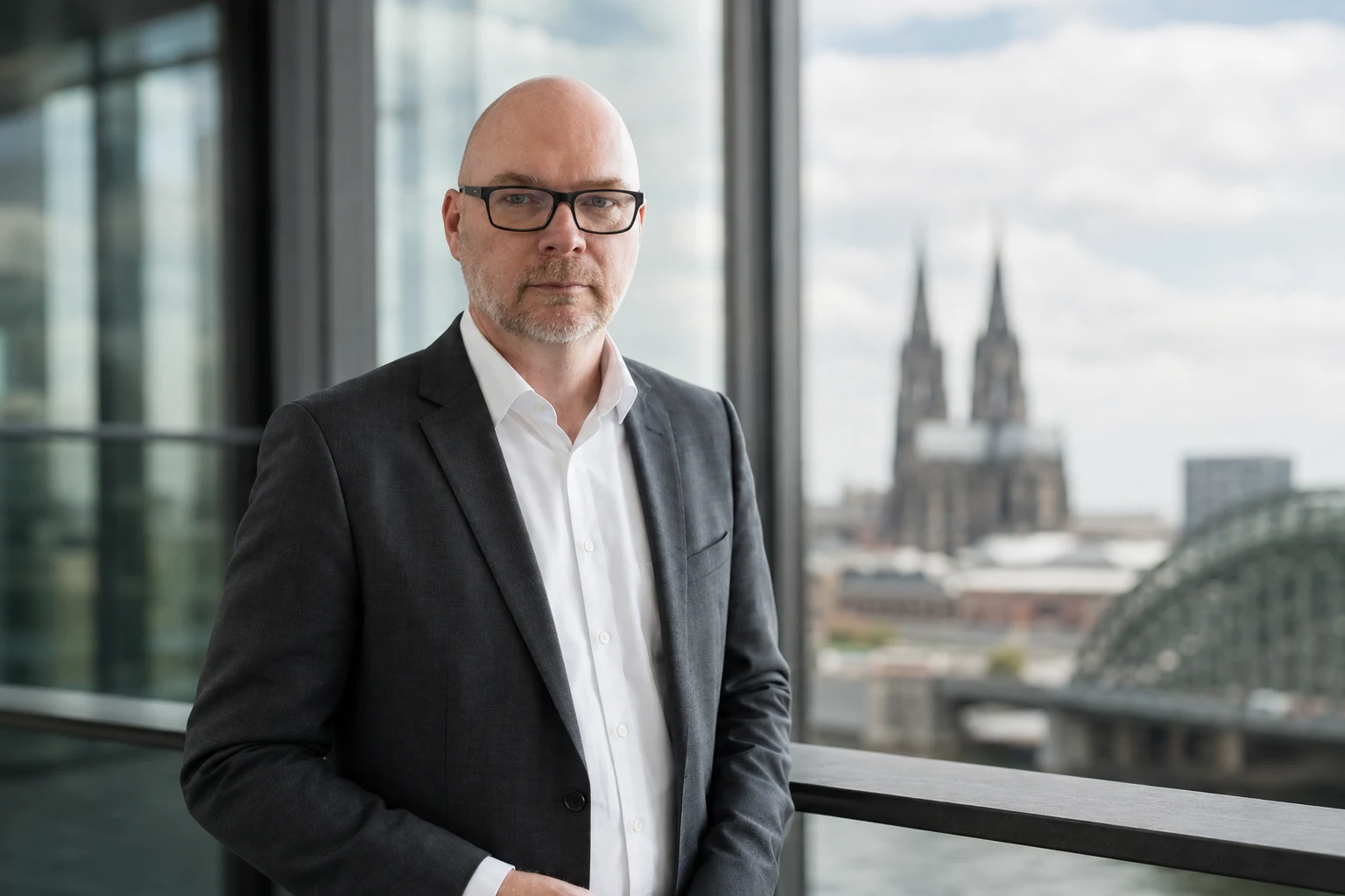 Stefan Budde-Siegel im schwarzen Sakko in einem Büro vor einer Kölner Stadtkulisse